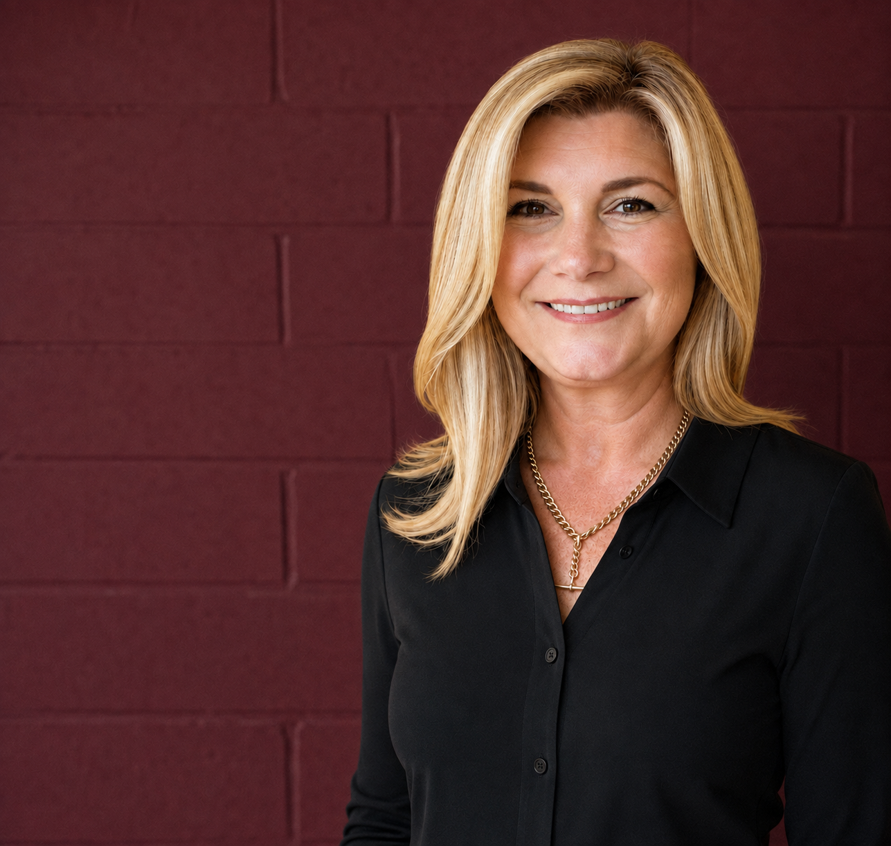 Professional headshot of Dr Gabrielle Morrissey in a black shirt and gold chain necklace against a plum studio wall