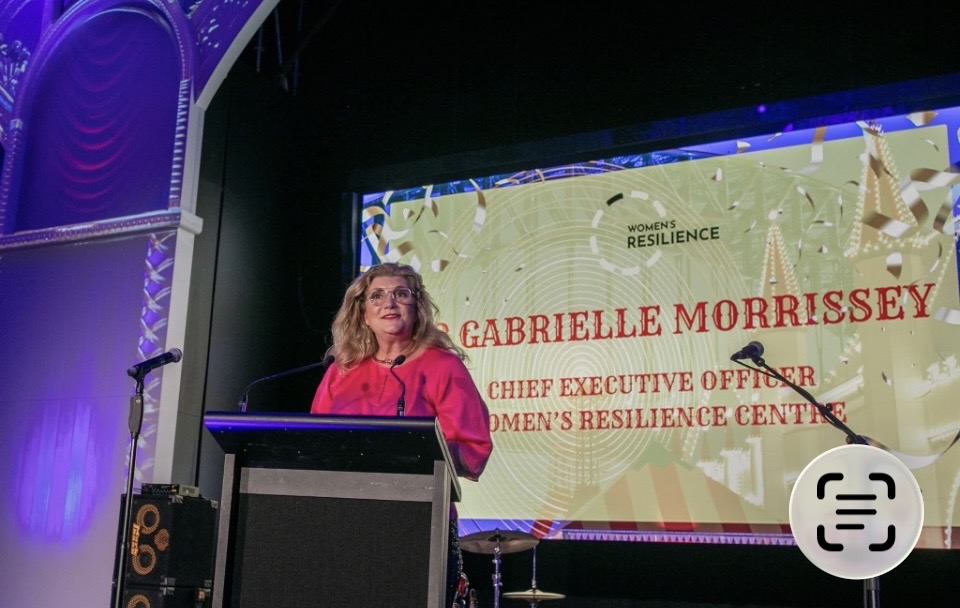 Dr Gabrielle Morrissey on stage beside a screen naming her as Chief Executive Officer of the Women's Resilience Centre